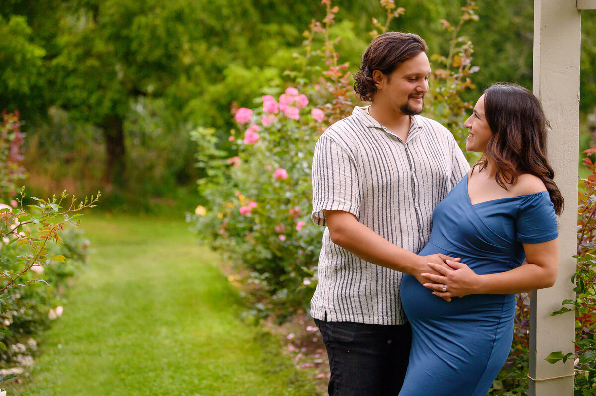 husband and wife in a rose garden for their maternity photos in Burlington, On