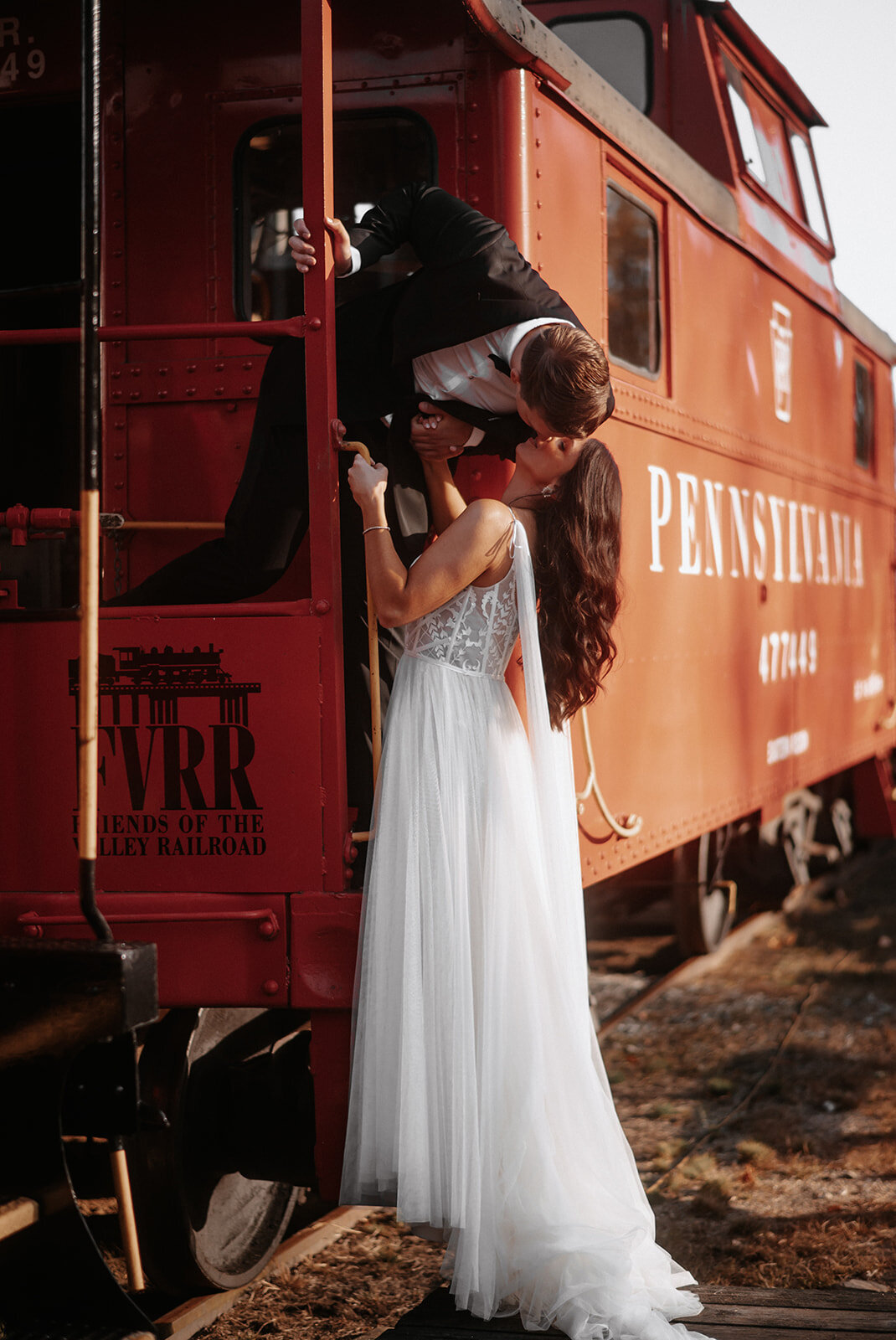groom stands on back of train and leans down to kiss bride at lace factory wedding photo by cait fletcher photography