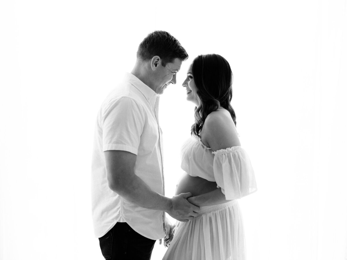 husband and pregnant wife in white two piece maternity gown holding baby bump for maternity photoshoot