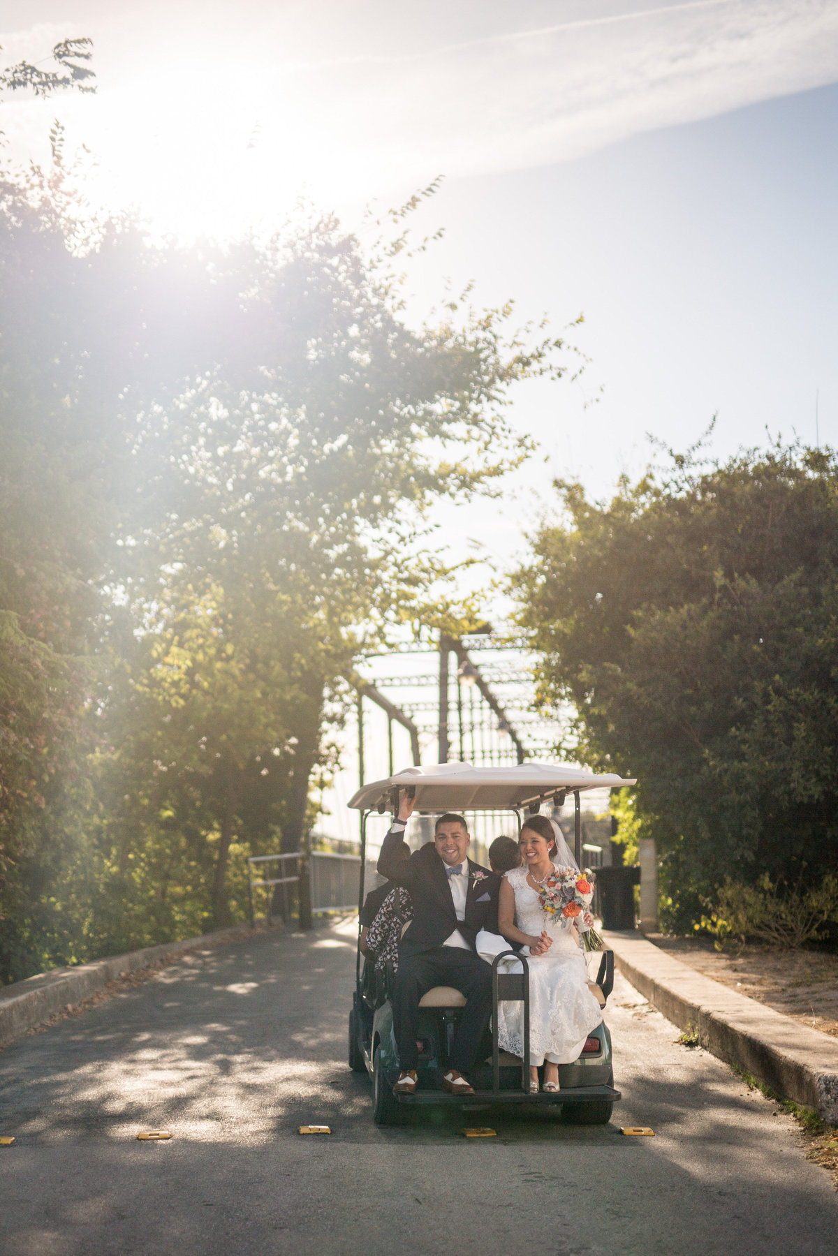 bride and groom sitting on golf cart after wedding ceremony heading to take pictures on bridge
