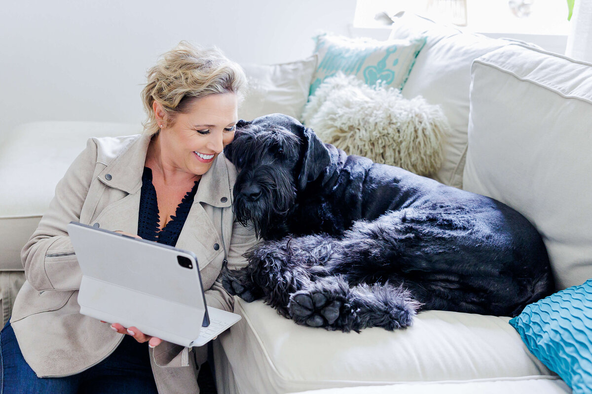 Lady snuggling with her dog as she works on her laptop
