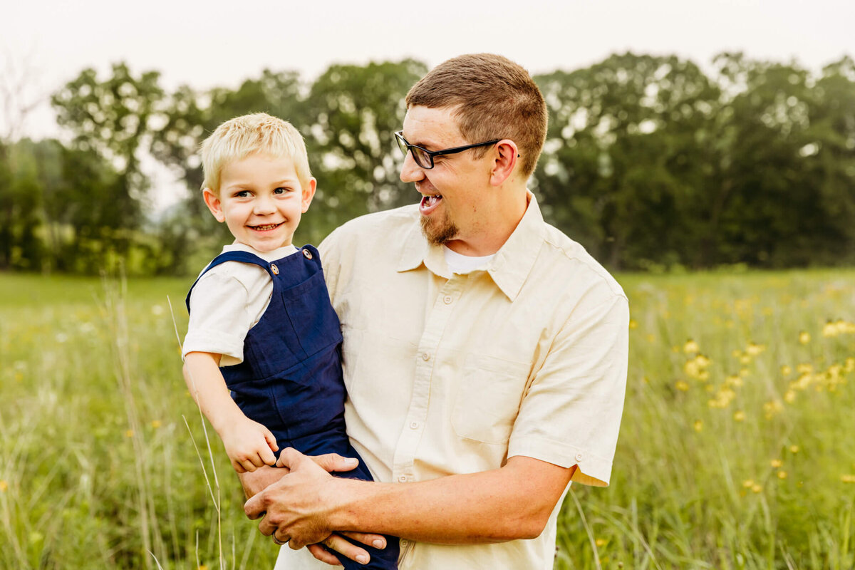 dad holding his son as they play and laugh in a field by Ashley Kalbus Photography
