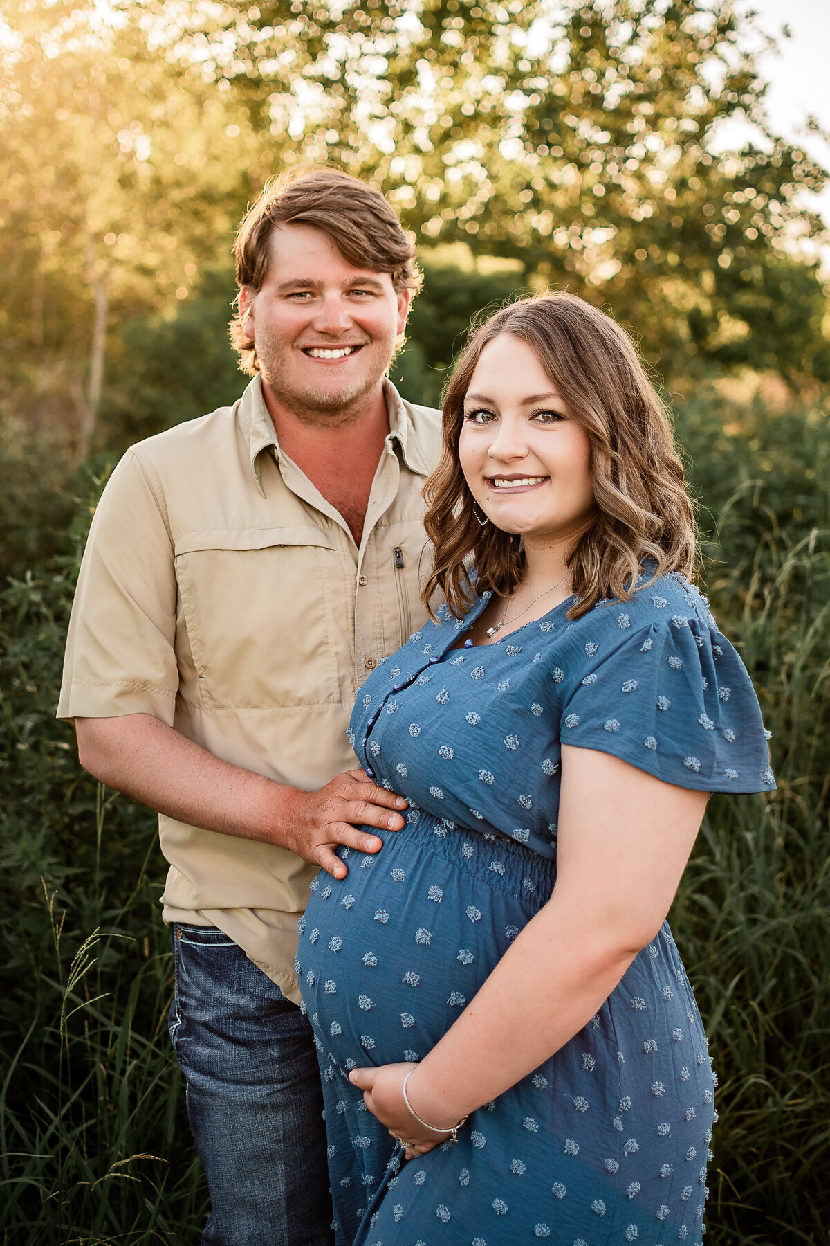 A mom and dad stand close and smile for their maternity pictures in Webster, TX.