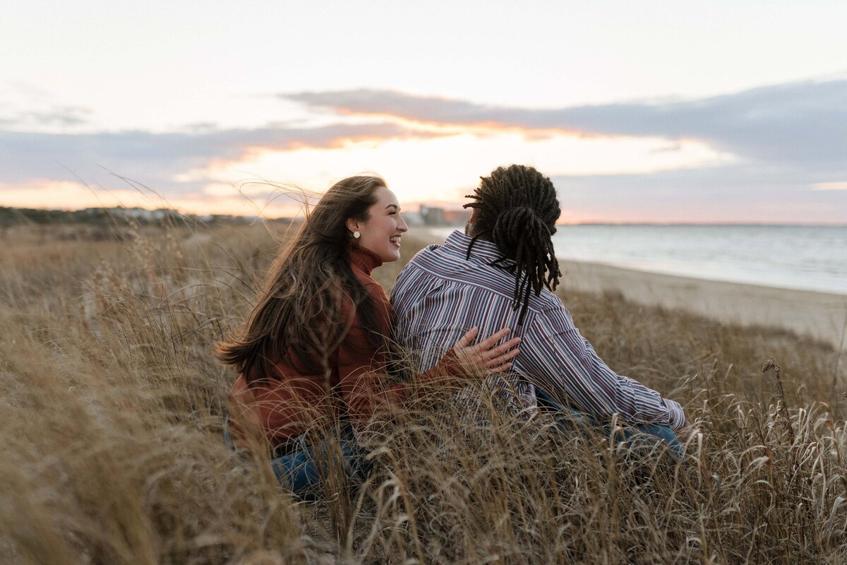 couple laughing and sitting along the shoreline in virginia beach