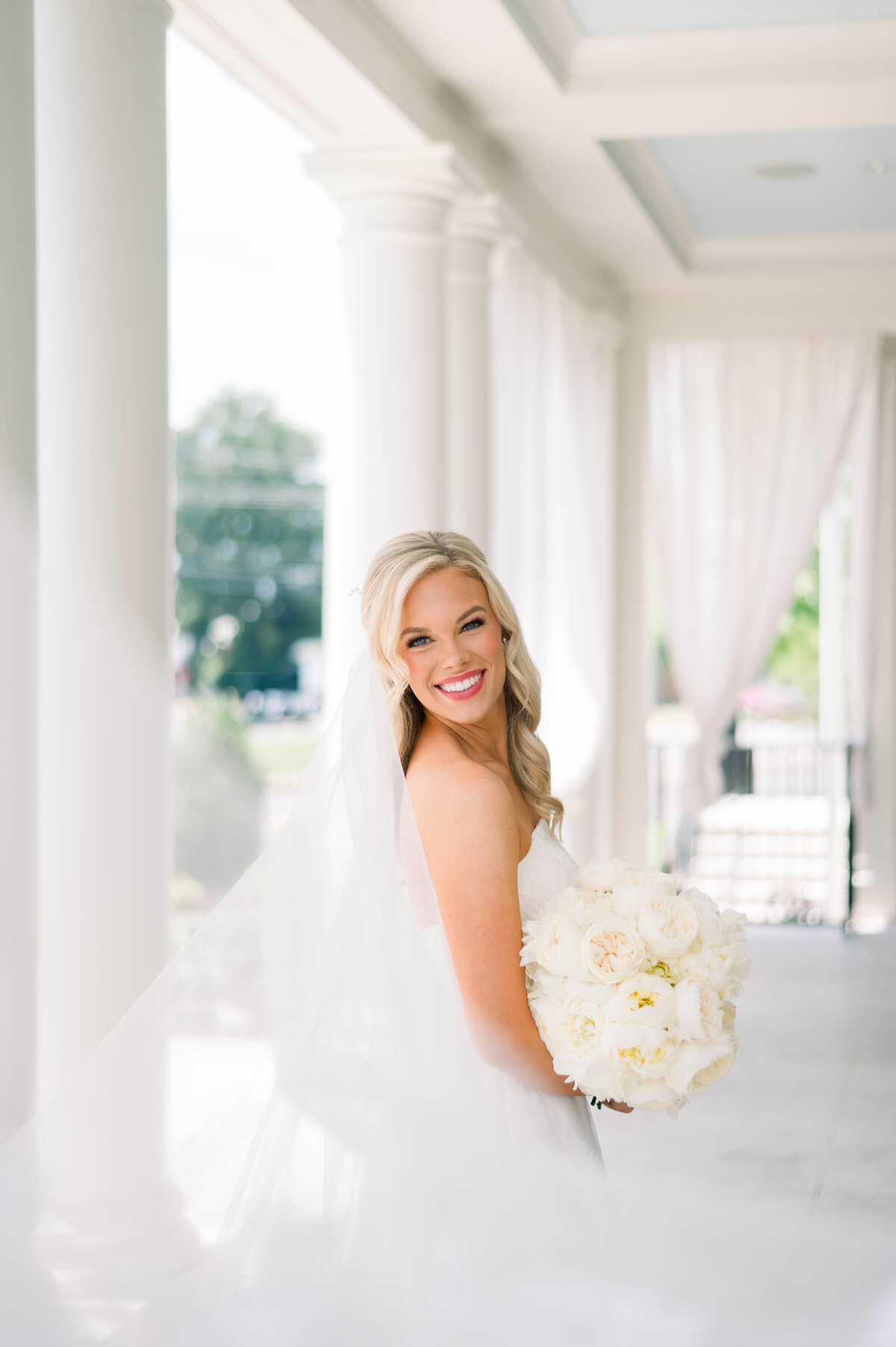 Bride in a Robert Bullock wedding dress standing on the veranda of the University Club in Tuscaloosa, Alabama during a romantic summer wedding
