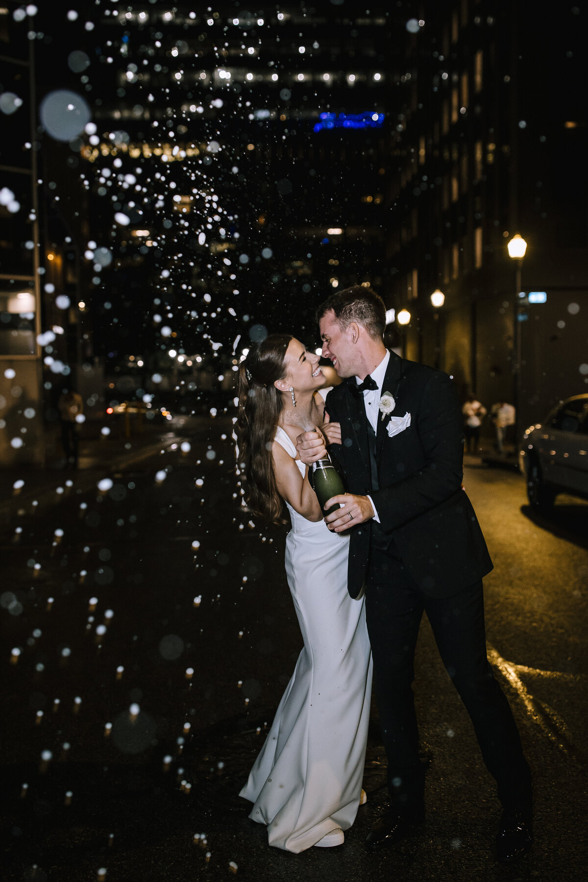 Bride and groom popping champagne and spraying at night in downtown Pittsburgh outside of the PPG Wintergarden. 