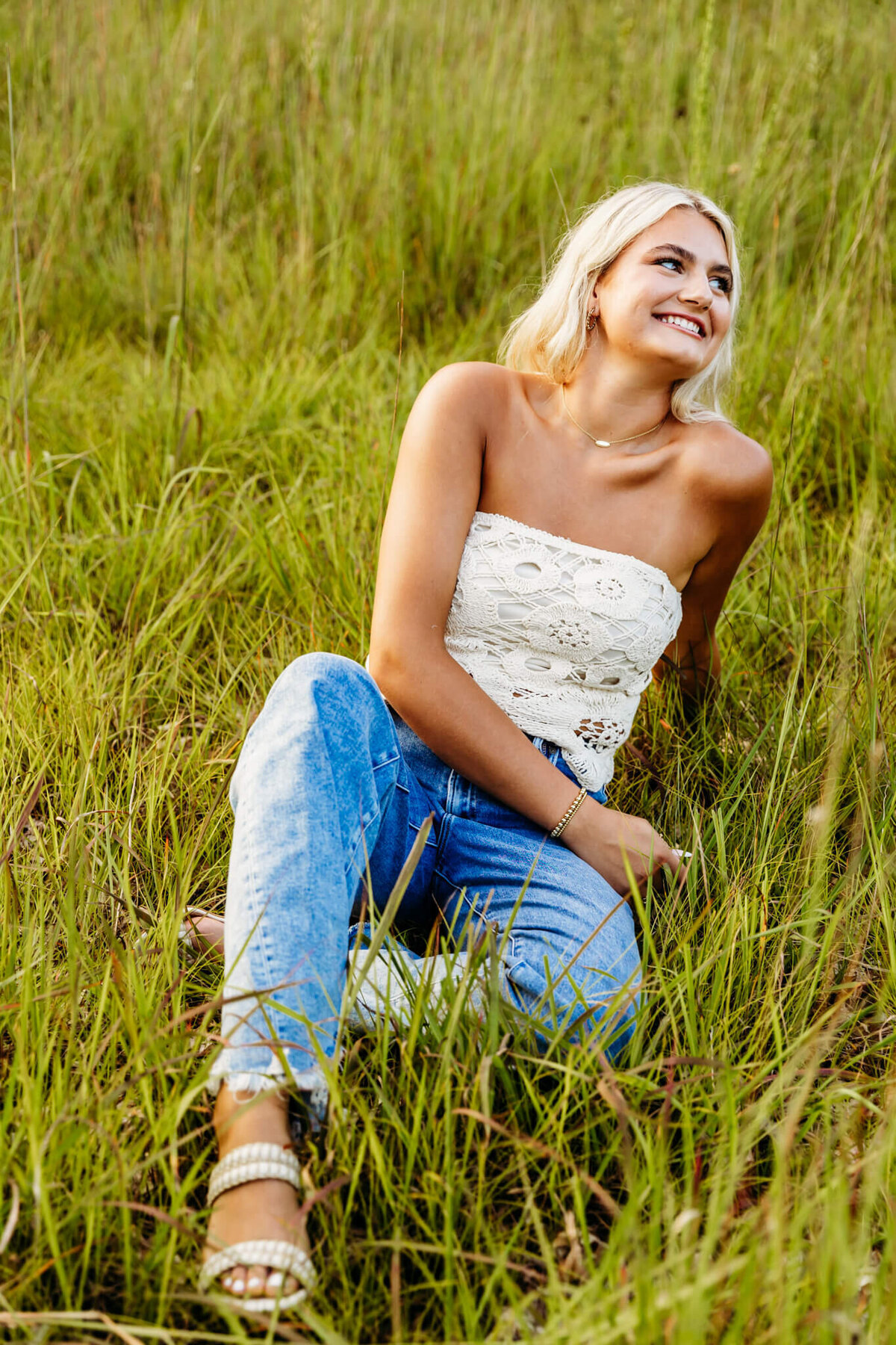 beautiful teenage girl from Neenah high school sitting in the grass and looking off to the side as she laughs 