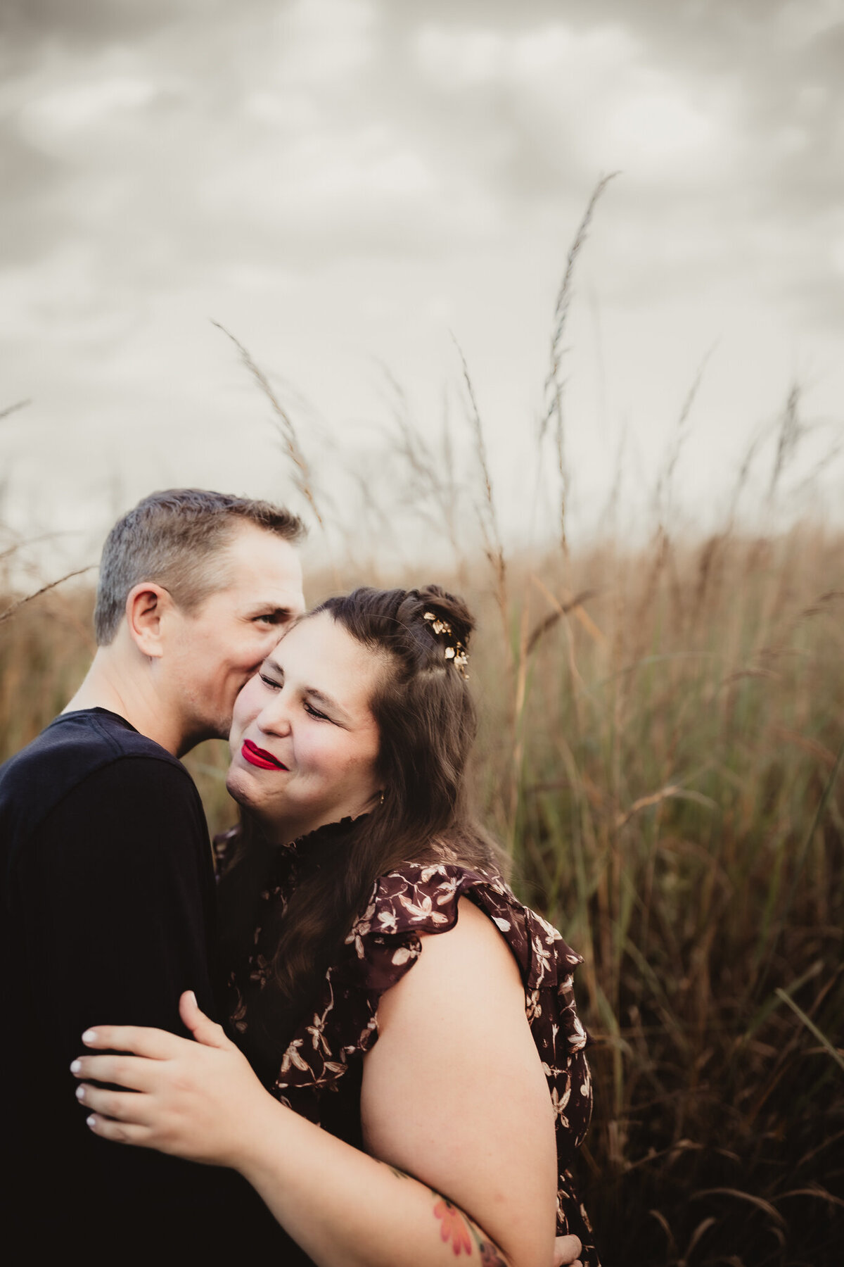 man and woman embracing with man kissing her cheek as she smiles