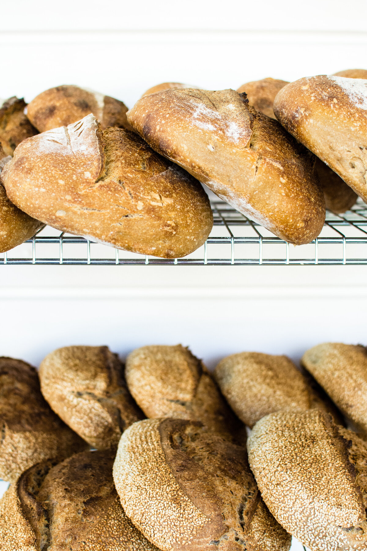 Two shelves filled with loaves of bread against a white wall