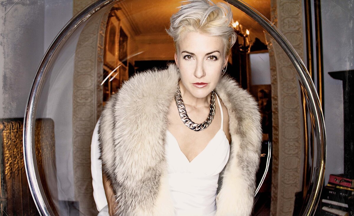Female musician portrait Tanya Legrossi  wearing white fur  coat silver  necklace sitting inside glass circle chair