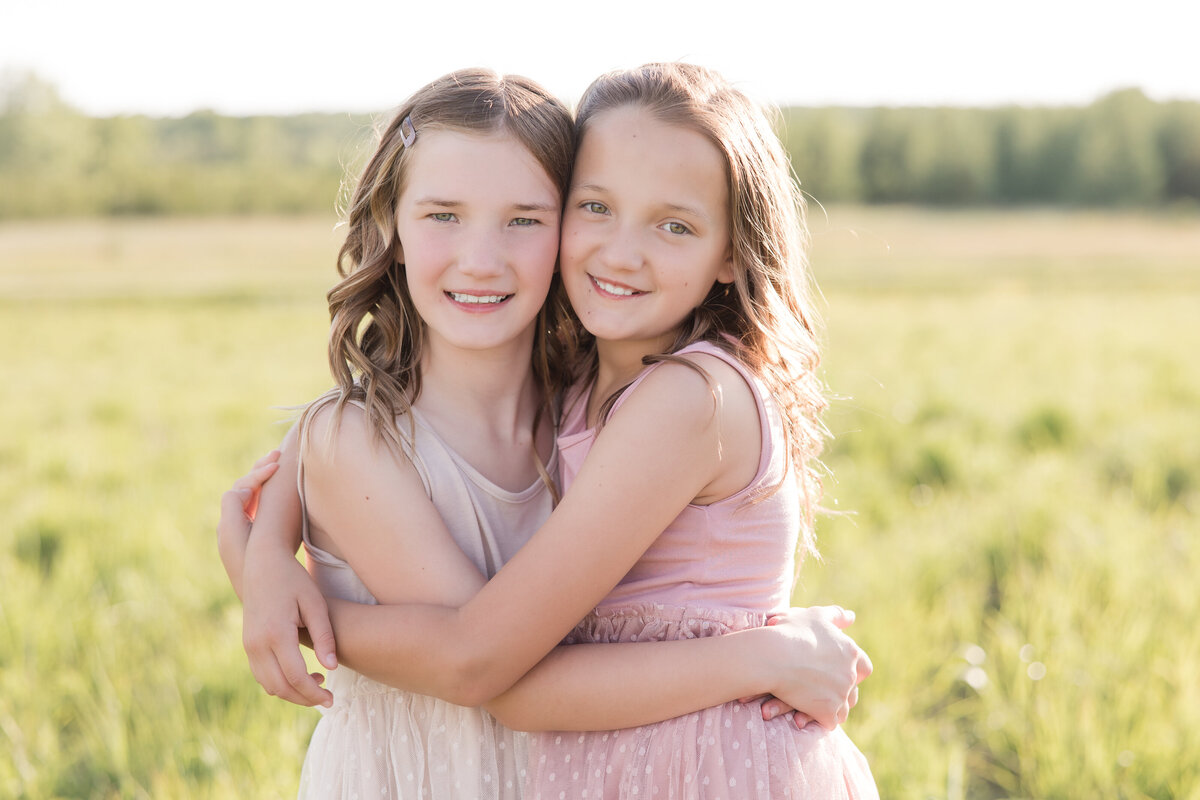 Two sisters are hugging in a field and smiling at the camera