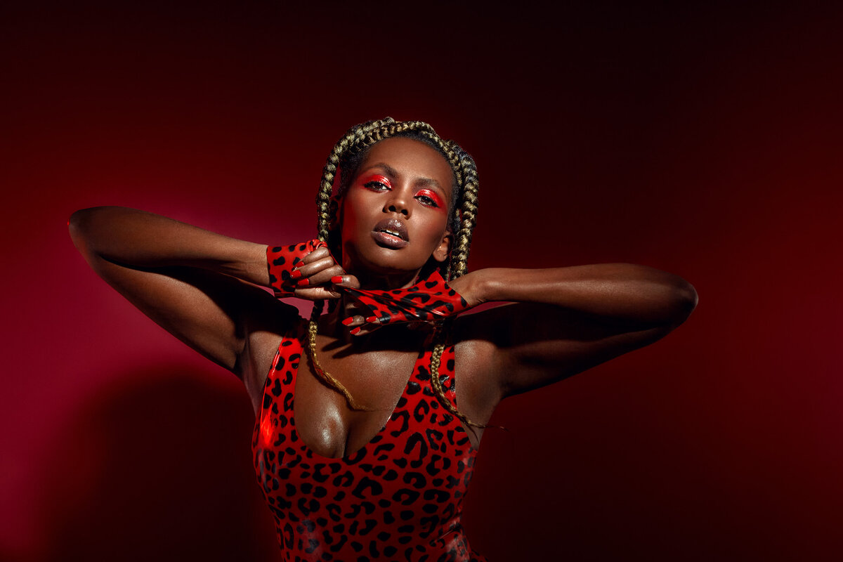 Powerful portrait of Lilian in a red leopard-print outfit and gloves, striking a confident pose against a deep red background, captured by Ylva Erevall.