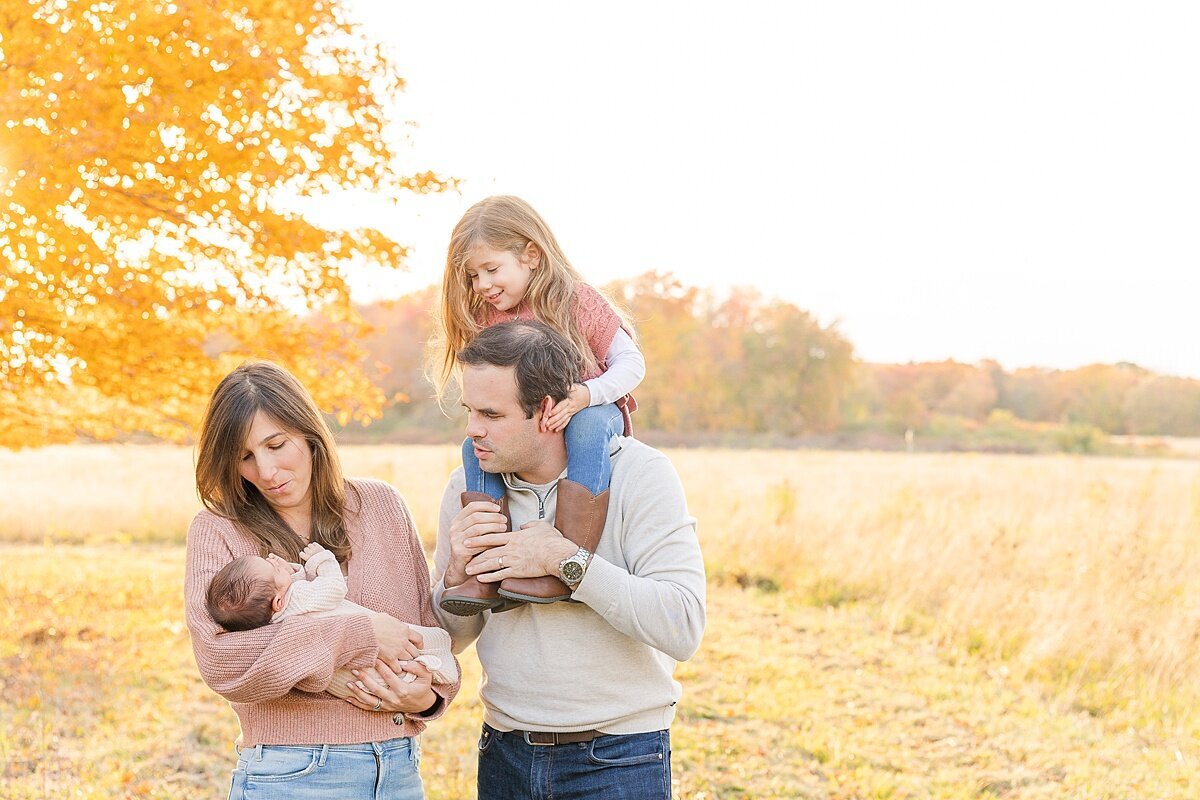 family stand by tree with fall foliage  during outdoor newborn photo session with Sara Sniderman Photography in Natick Massachusetts