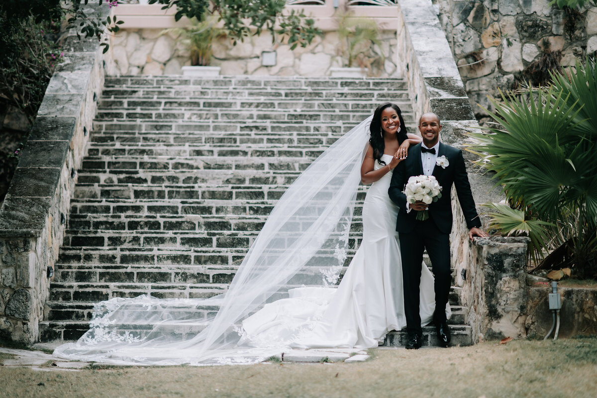 Handsome groom & bride with long veil on steps in the the Bahamas