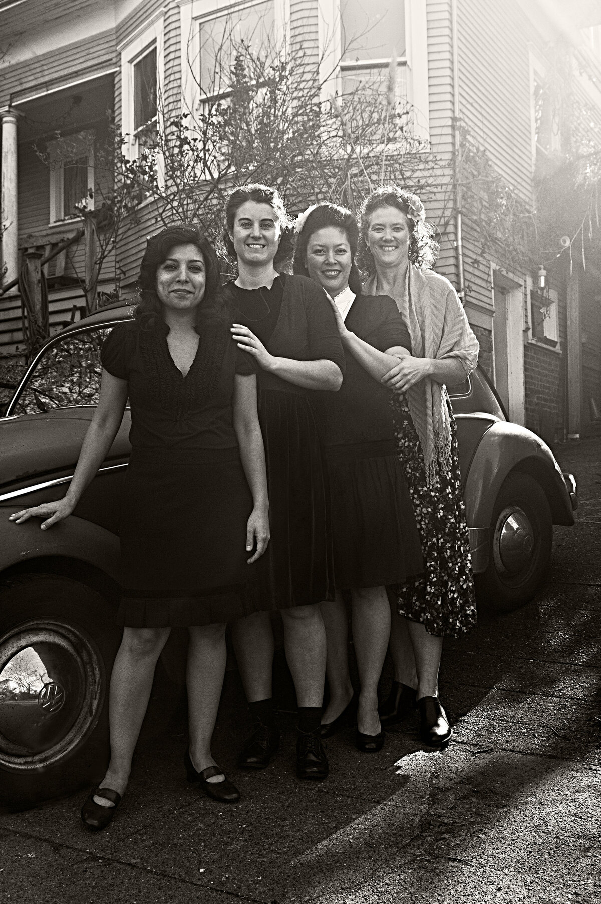 A group of women smiling and standing next to a vintage car