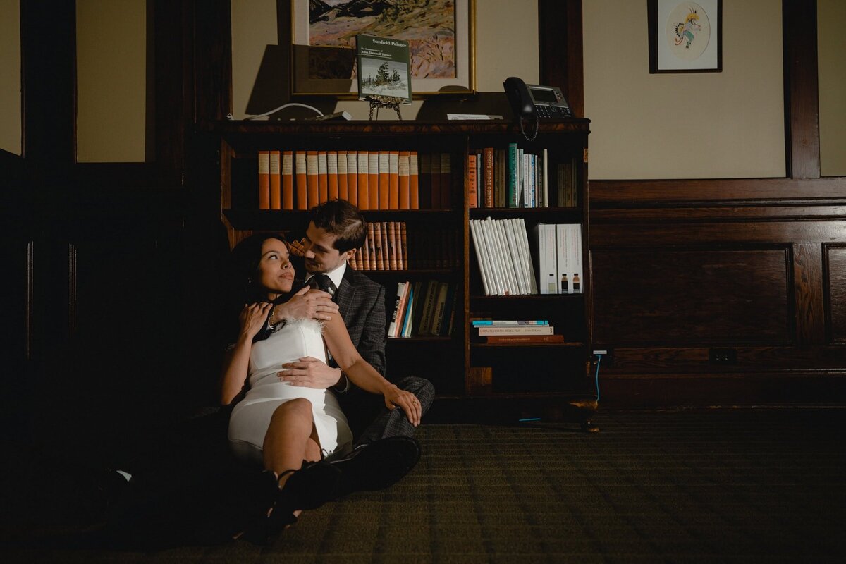 Engaged couple look at each other in front of fancy old-fashioned bookshelf at The Ranchmen's Club in Calgary
