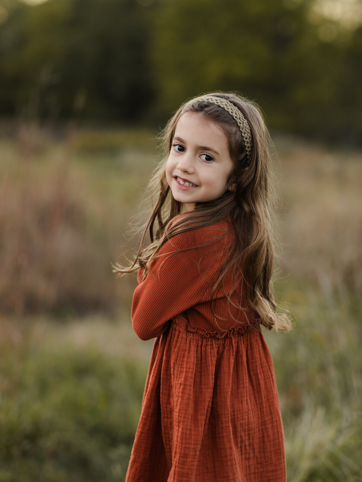 girl in rust colored dress posing for family photos in field 
