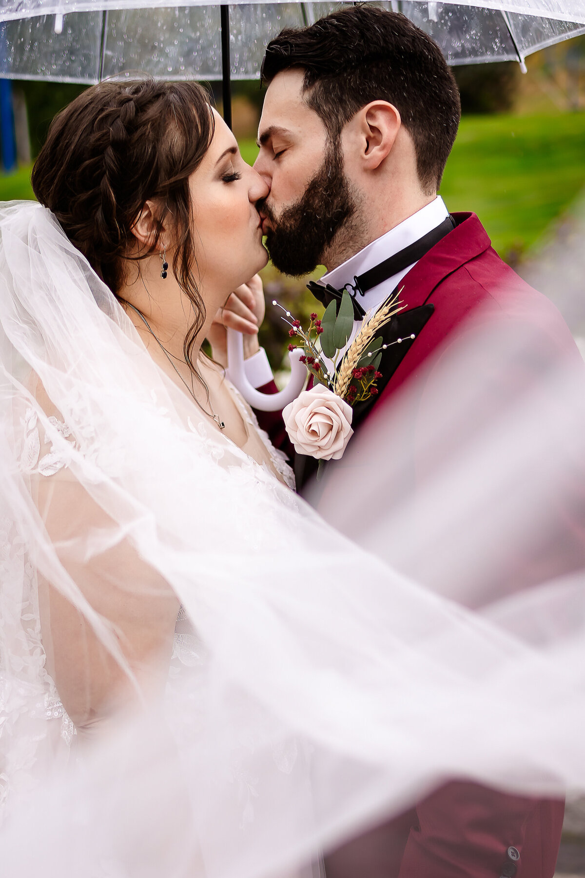 bride and groom kissing under an umbrella as vail swoops across them in sweet intimate moment