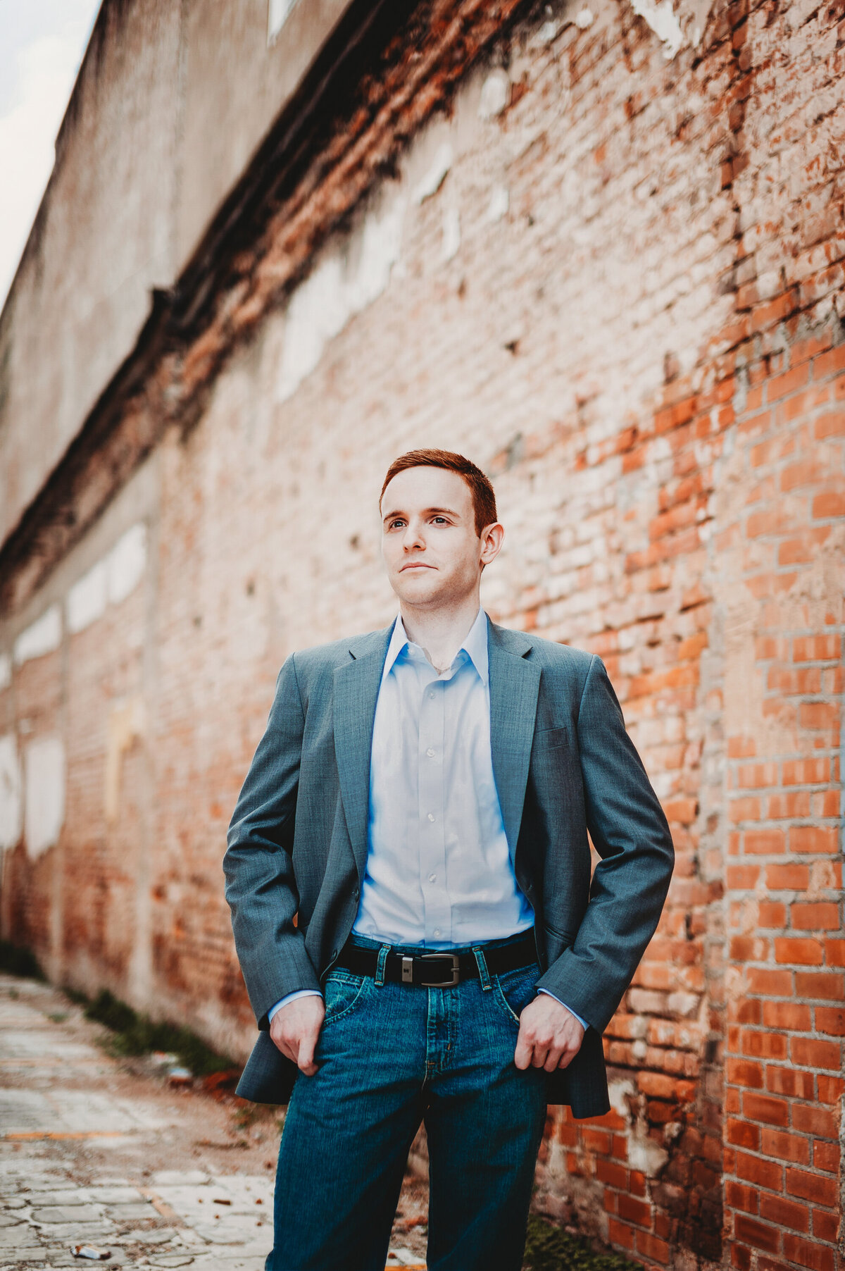 Man posing in a suit jacket against a rustic brick wall during an outdoor portrait session in Orlando Florida.