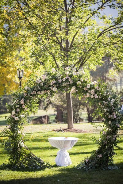 A circular wedding arch is adorned with greenery and white roses.