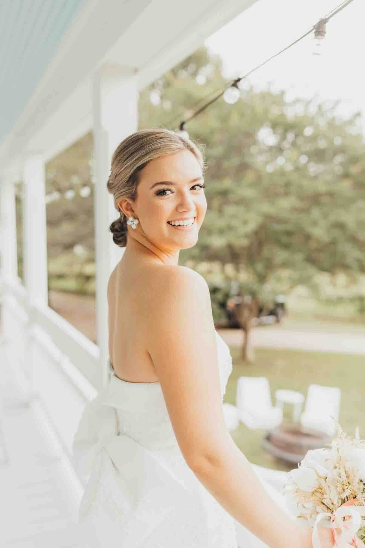 bride looks over her right shoulder at ally's photography while standing under white porch.