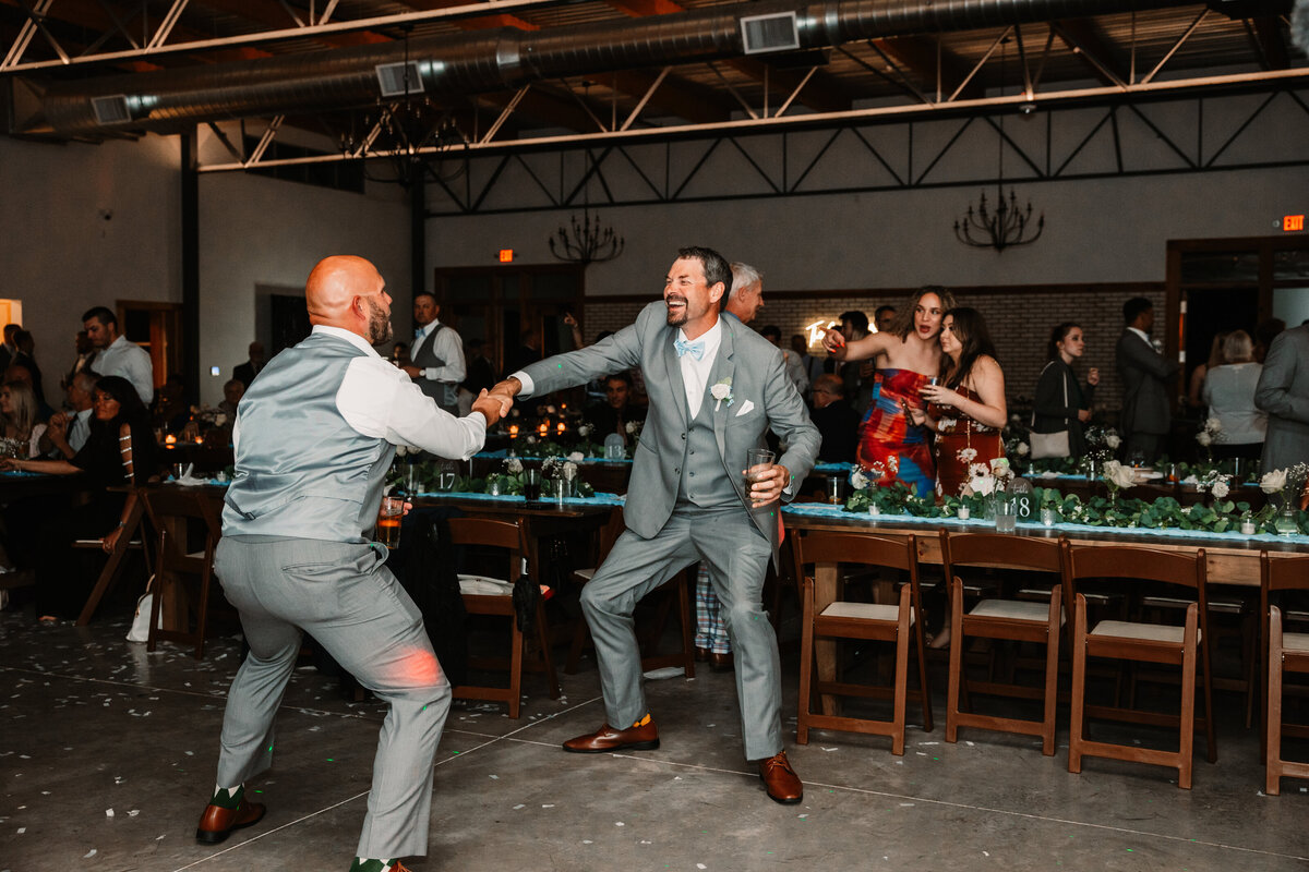 Two groomsmen dance and hold hands during the reception on the dance floor