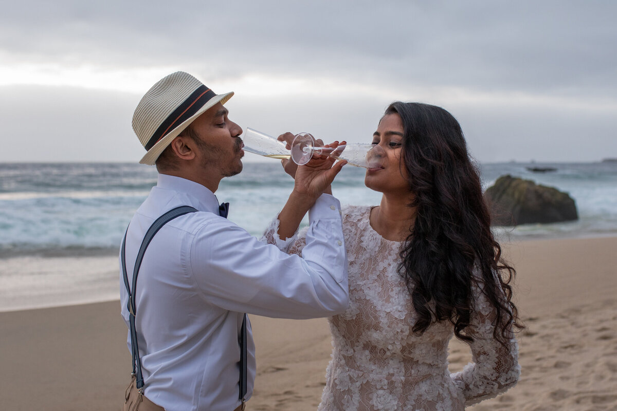 A bride and groom drink champagne on the beach in Big Sur.