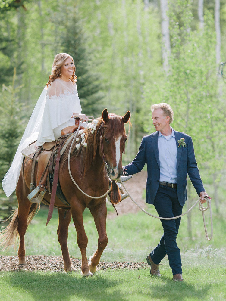 Bride riding in on a horse at a Colorado ranch wedding