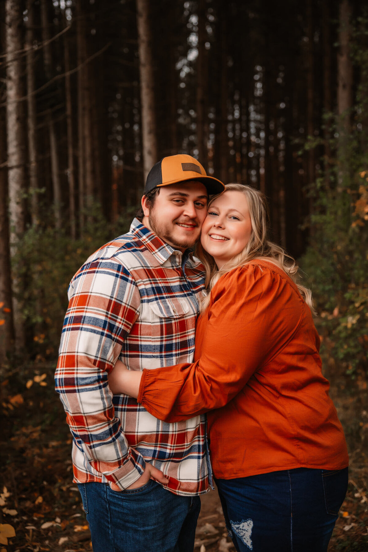 man and woman snuggle and smile at camera in forest