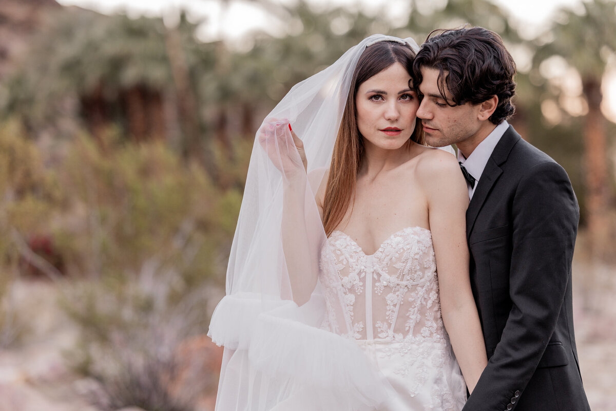 Bride leaning on groom’s shoulder in soft desert lighting.
