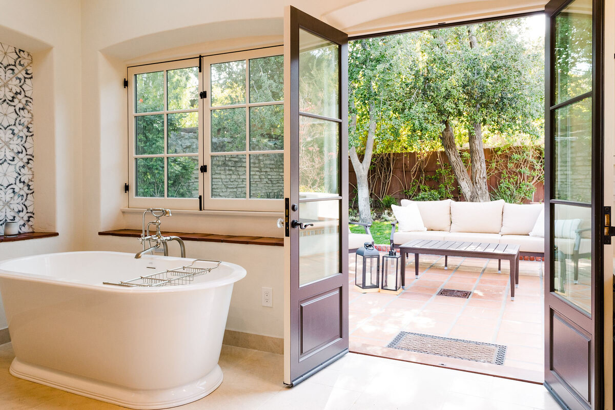 bright and airy trasitional bathroom with a view to a lush designed backyard. a standing tub with antique looking hardware. french doors and ornate tiles to add a refined look to this master bathroom.