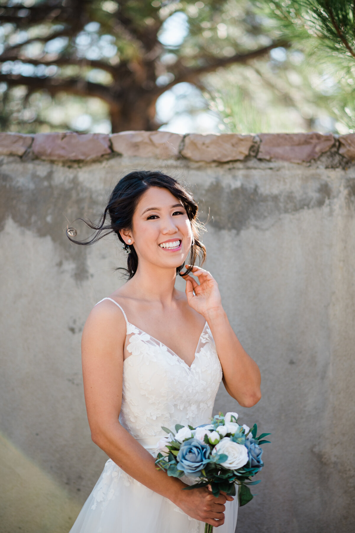 Denver wedding photographer captures a bride smiling at the camera while holding her bouquet and moving her hair to the side with her other hand