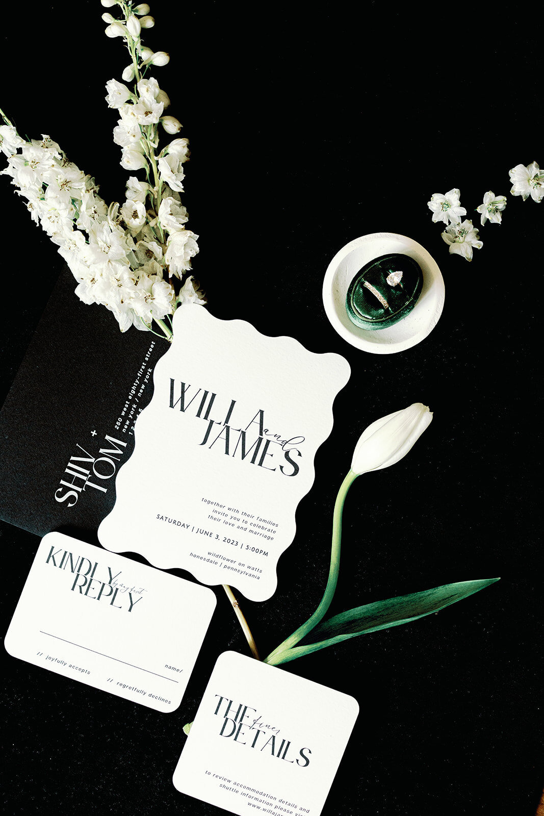Scalloped wedding stationery and wedding rings on a black background