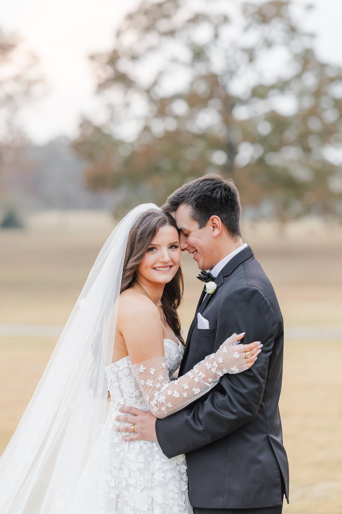 A groom nuzzles his bride's temple while snuggling in a field