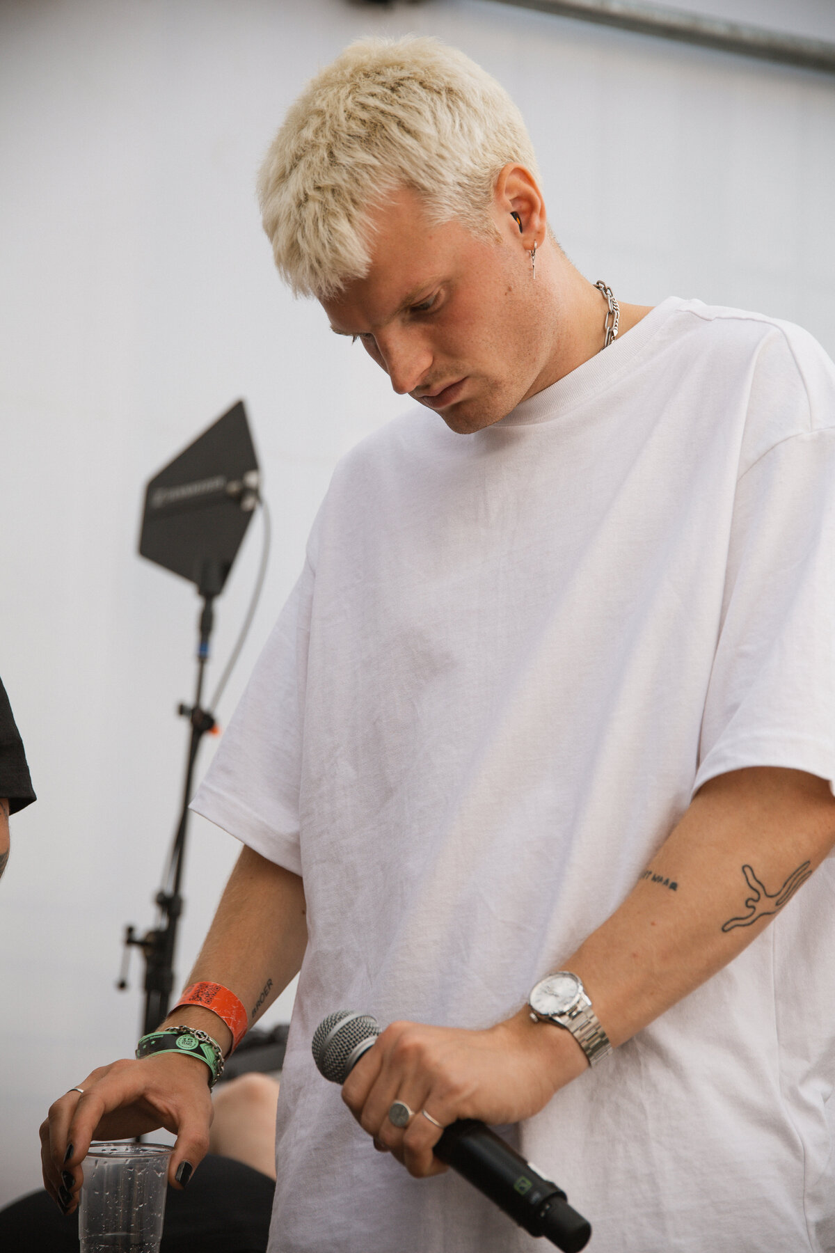 Sam Hofman is performing on stage, holding a microphone as he engages with the festival crowd. His arm is extended, and he looks focused on the moment, with the audience cheering and waving hands in the background. The energy of the performance is palpable in this vibrant and lively capture. (Photo by Bo Eppink)