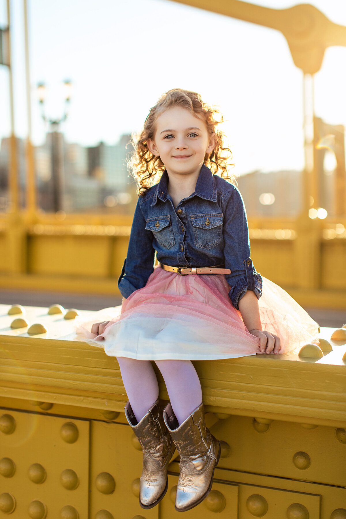 A blonde curly haired girl sits on the Roberto Clemente bridge in downtown Pittsburgh during a styled photography session with larger than life photography