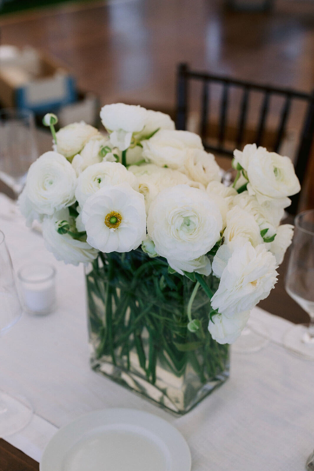 A centerpiece of white flowers in a glass vase on a dinner table for a wedding at Cape Cod Summer Tent, MA.