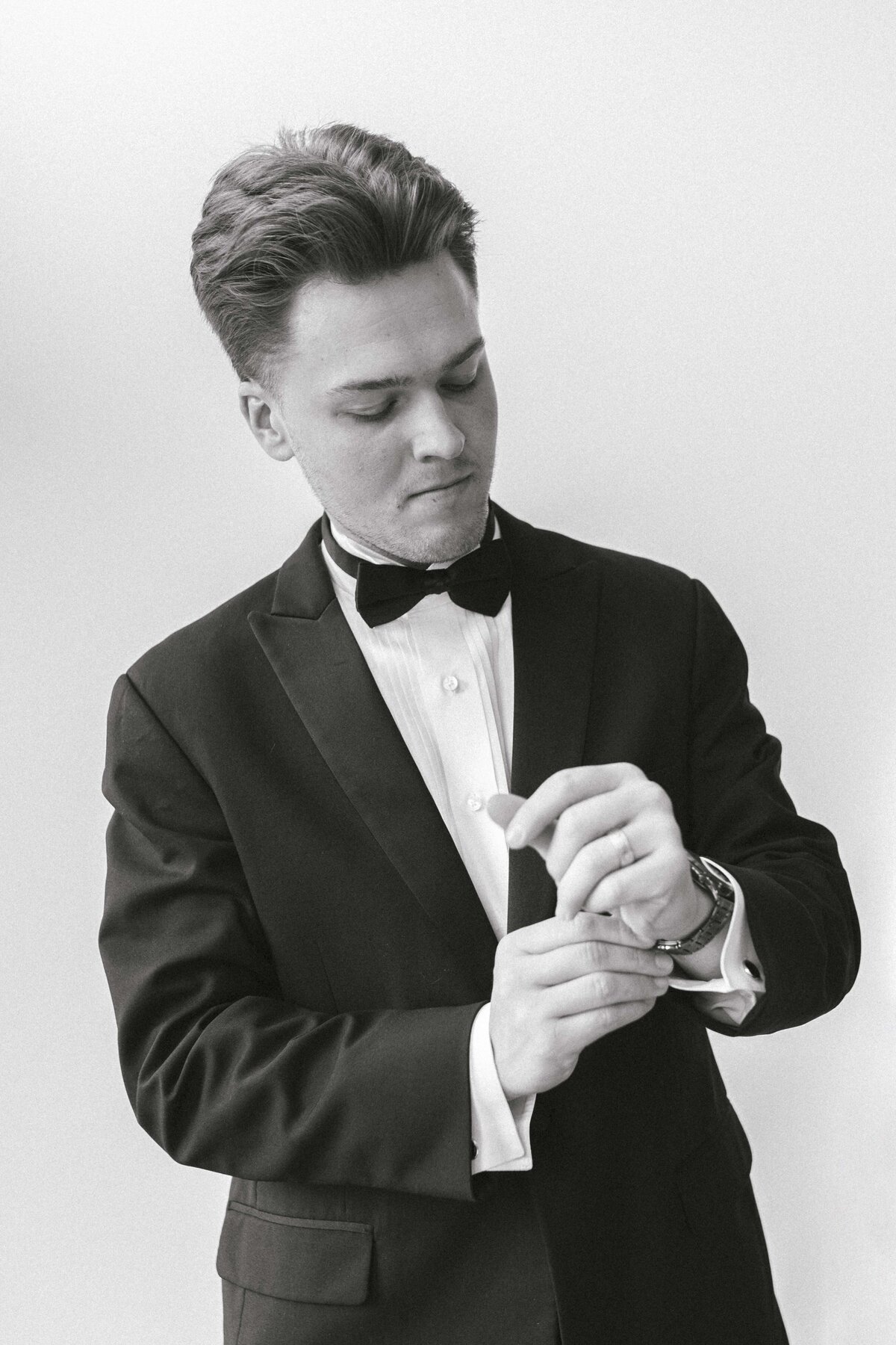 Black and white grooms portrait featuring groom fixing cuff links at wedding venue in Missouri