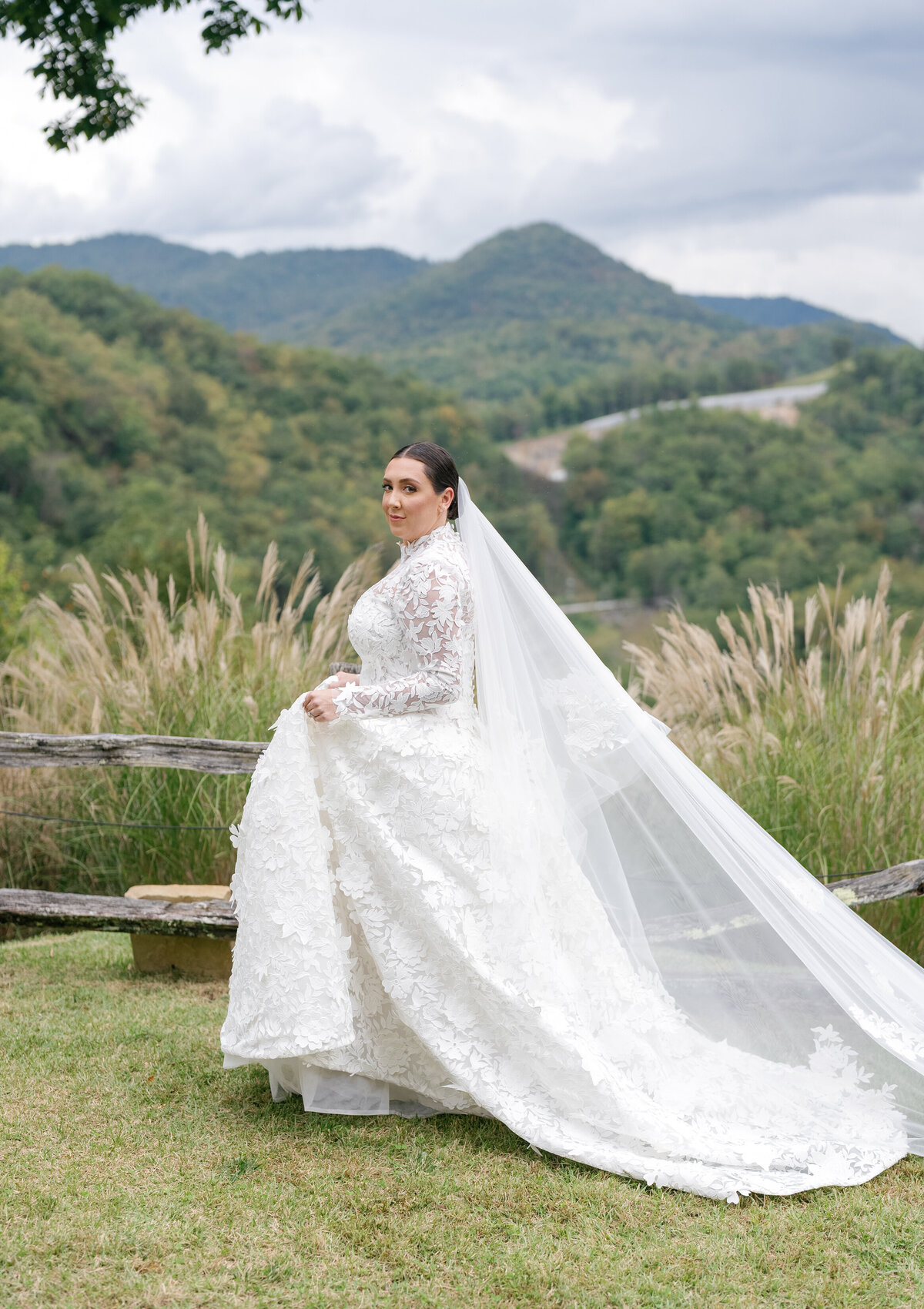 Bride in a long-sleeve lace wedding gown standing before sweeping Blue Ridge Mountain views during a luxury fall wedding at Castle Ladyhawke in Tuckasegee, North Carolina.