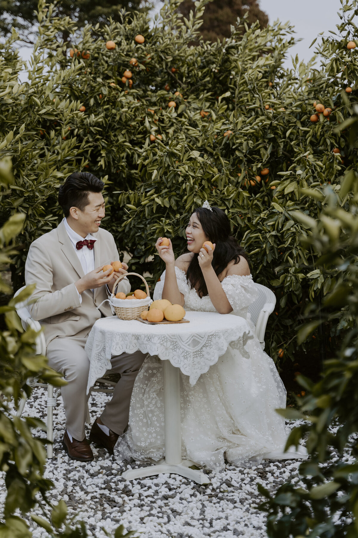the couple laughing while sitting in a table surrounded by tangerines
