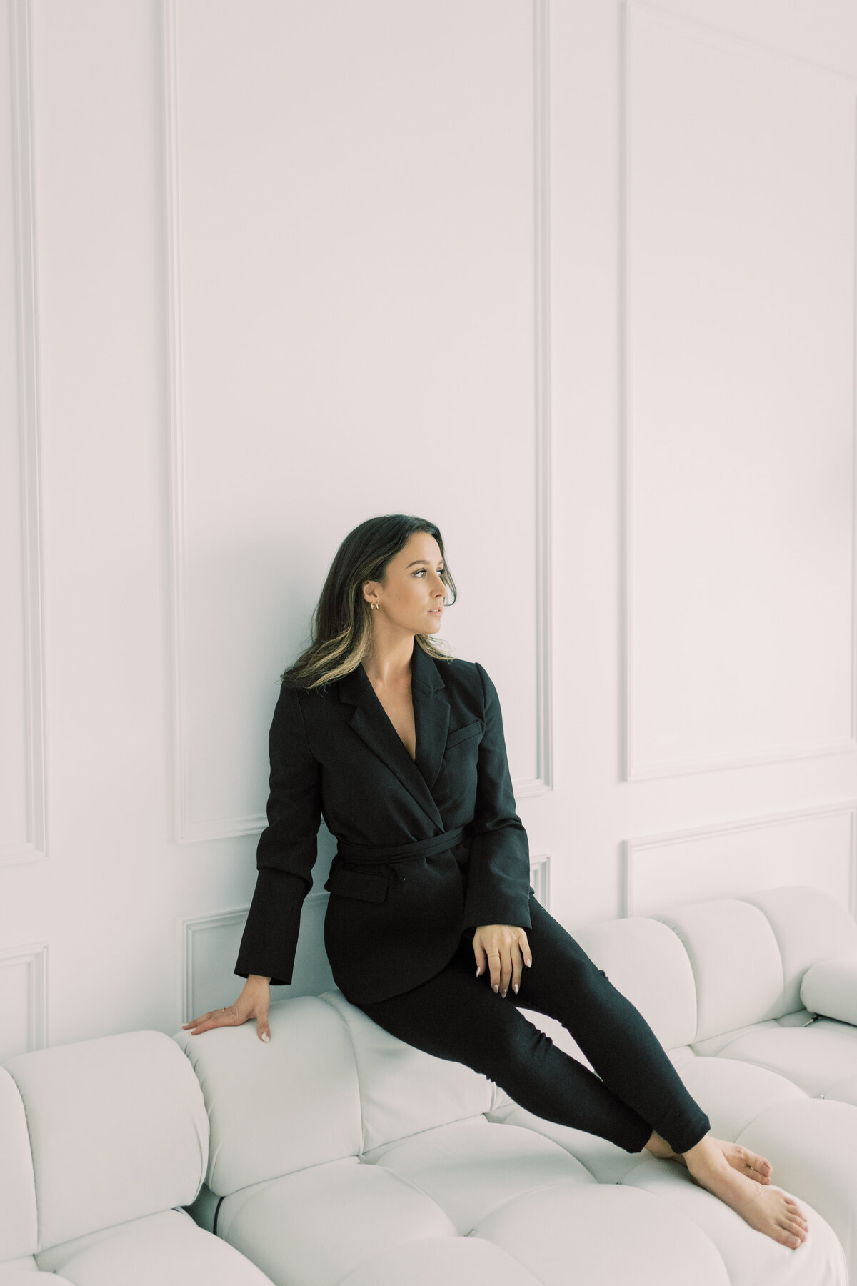Relaxed yet polished portrait of spa manager in black, seated in a minimal studio
