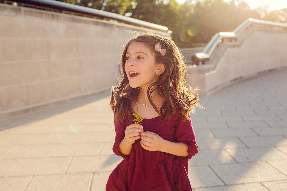 Girl is bouncing, happily looking to the side, flower in hand.