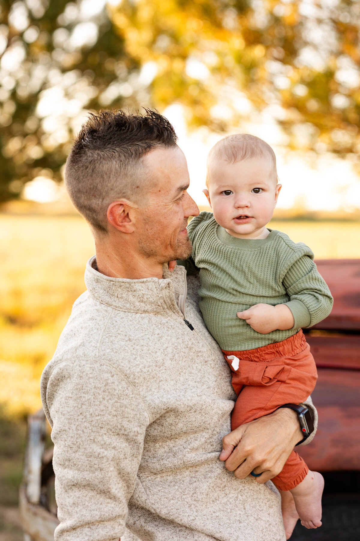 A dad holds and smiles at his baby boy while baby looks at the camera.