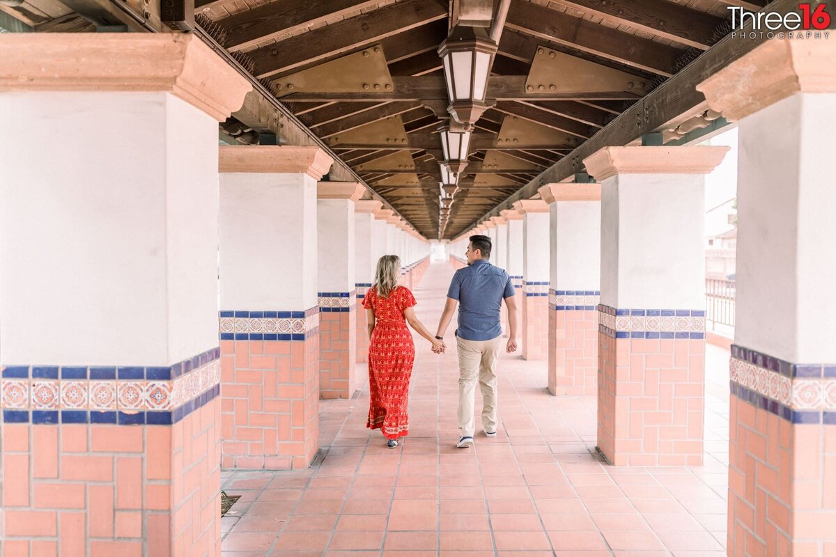 Engaged couple hold hands as they walk through the Santa Ana Train Station