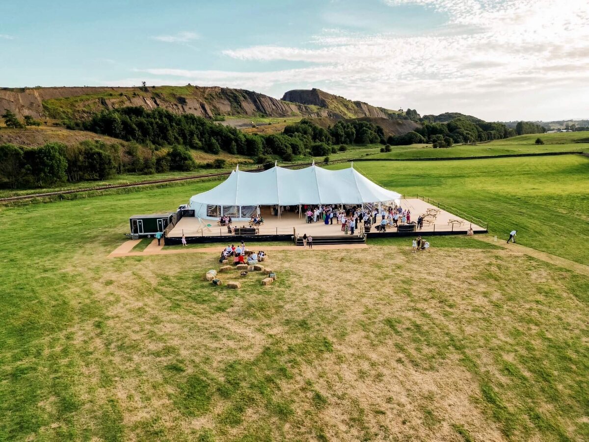 A large pole marquee in a field behind a lake with stunning country views