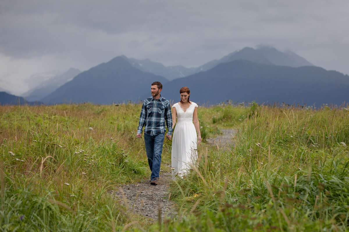 A bride and groom walk down a dirt path after their Alaska elopement ceremony.