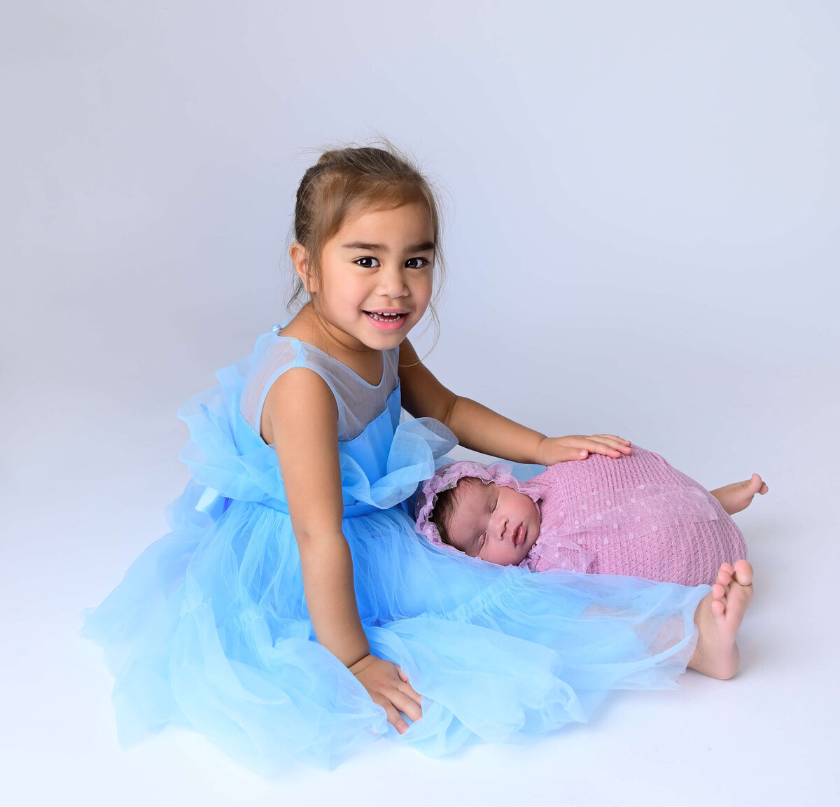Newly big sister holds her newborn sister in her lap for newborn portrait session. Image by Kitsap County, WA photographer Beth Benecki of E. Benecki Photography