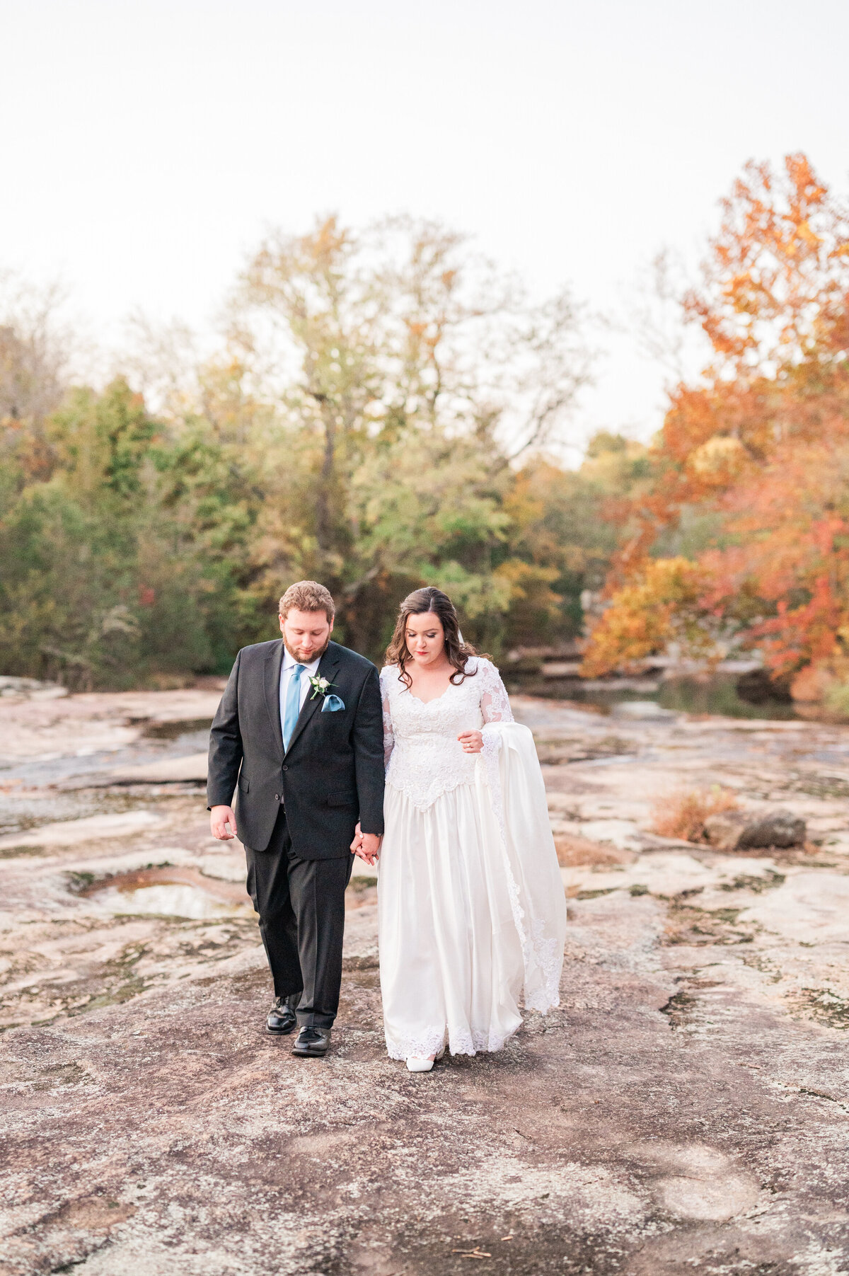 A newlywed couple holding hands and walking along rocks