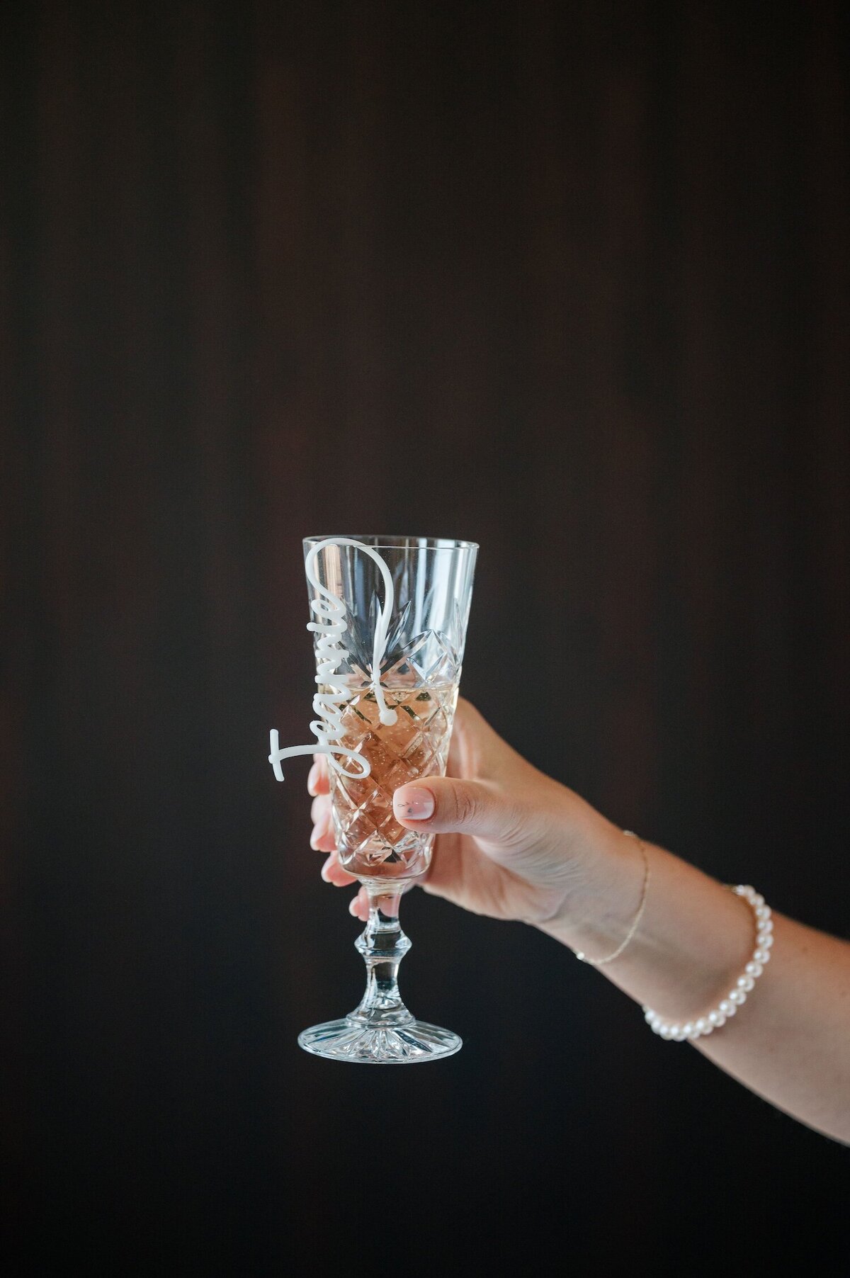 A hand holds up a champagne glass against a dark backdrop. 