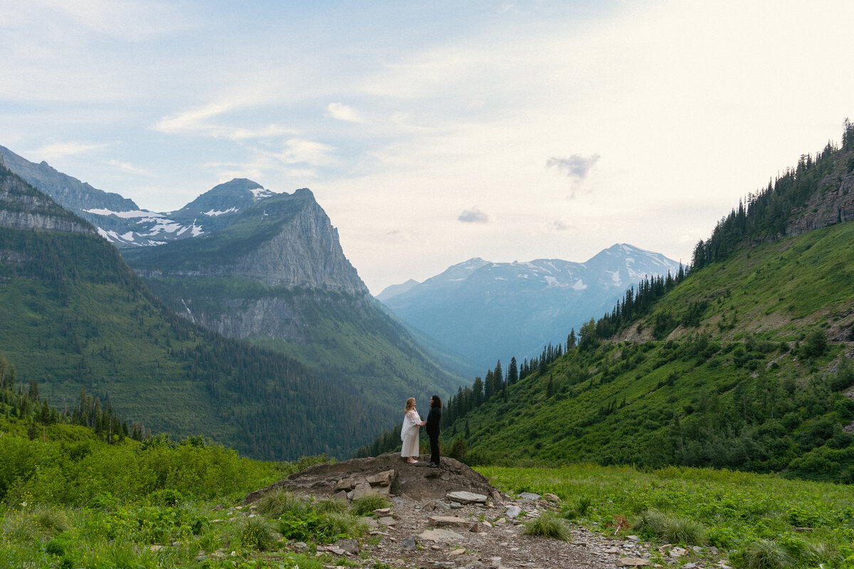 Couple hold hands in the middle of Glacier National Park mountain scenery.